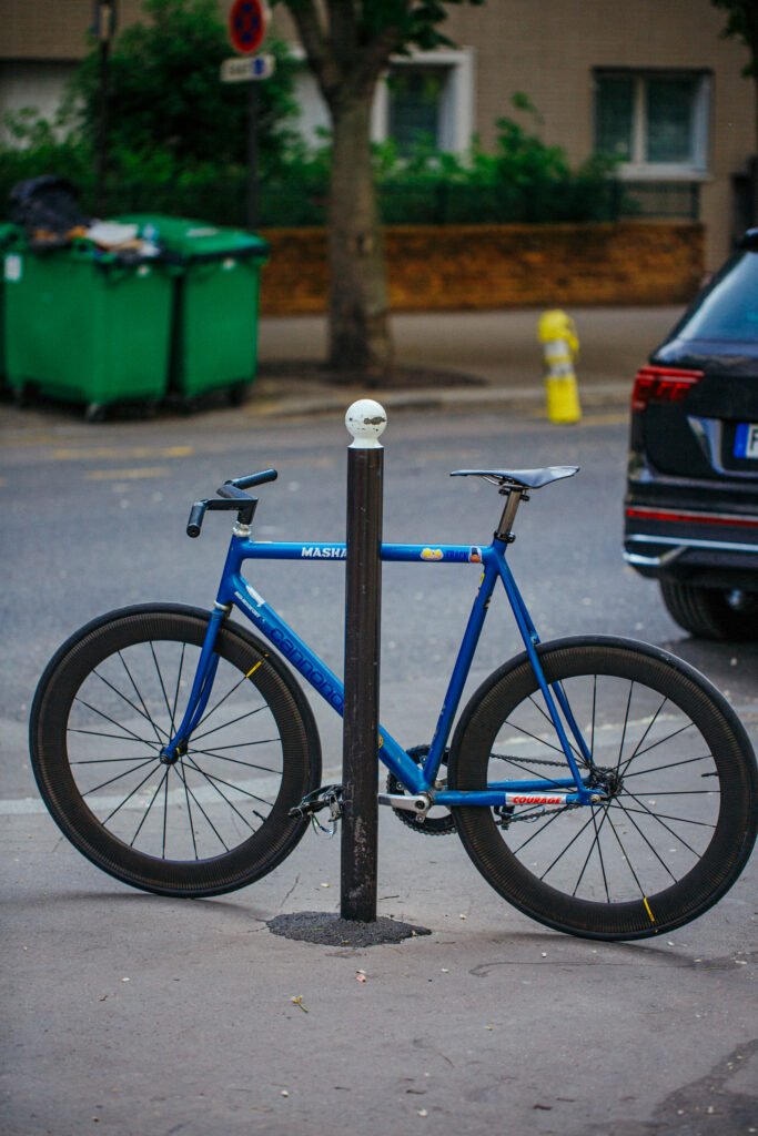 Pignon fixe bleu appuyé contre un potelet dans la rue.