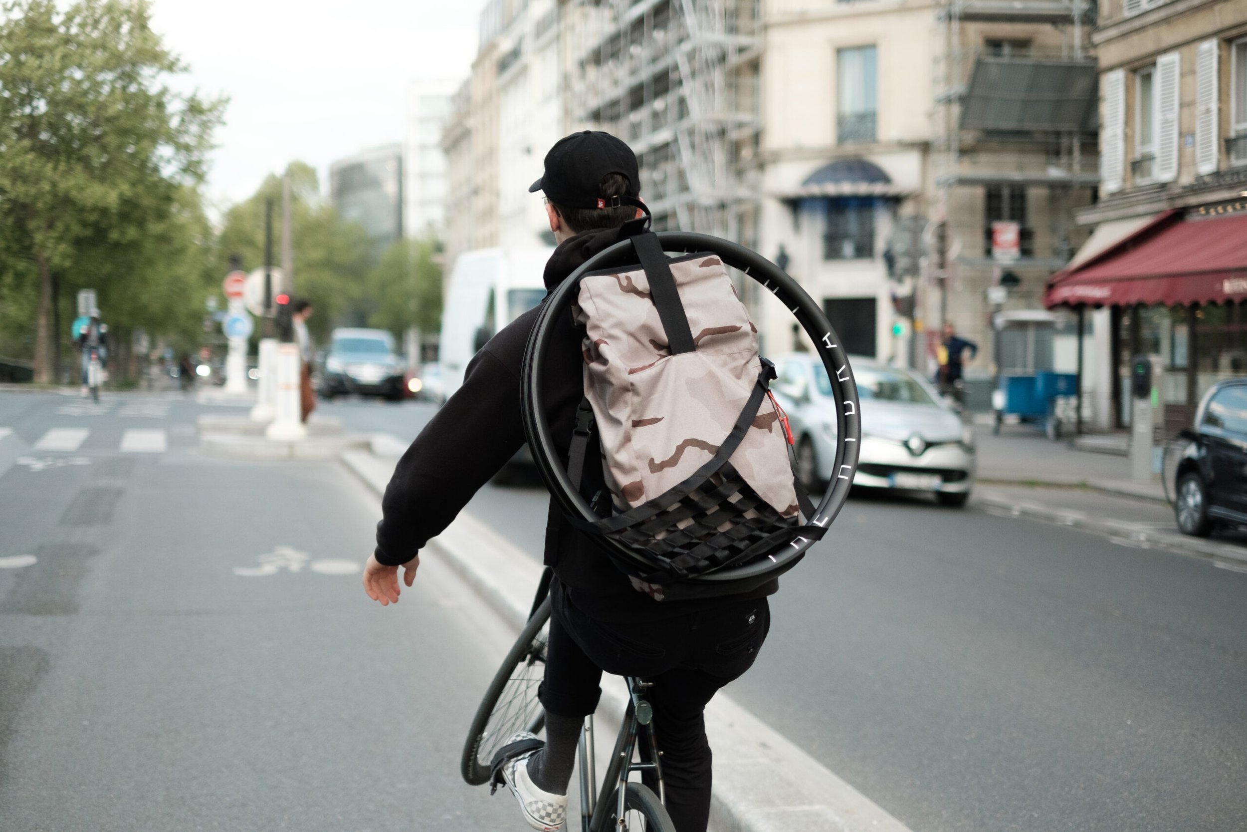 Rider traversant la rue à vélo avec une paire de jantes sur son sac à dos.