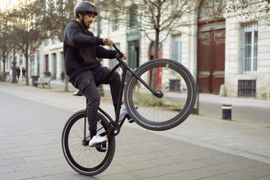 Rider en wheelie sur un vélo noir sur une place bordée d’arbres.