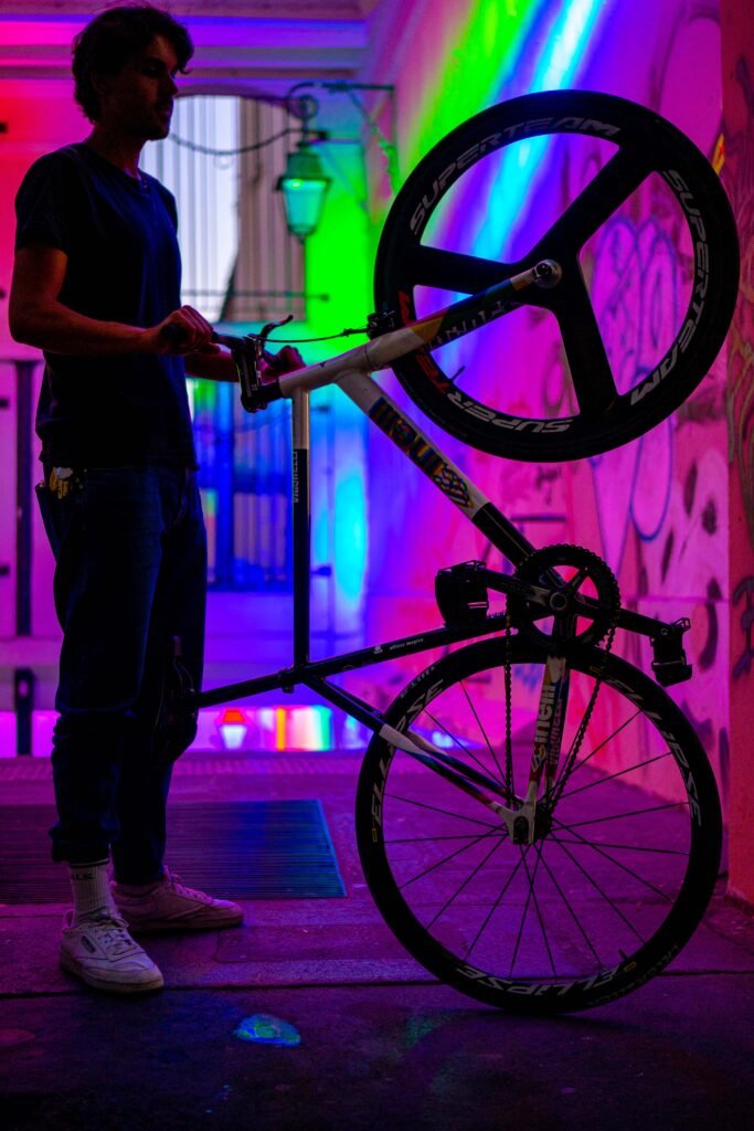 Rider tenant la roue avant d’un vélo en l’air dans un passage aux lumières colorées.