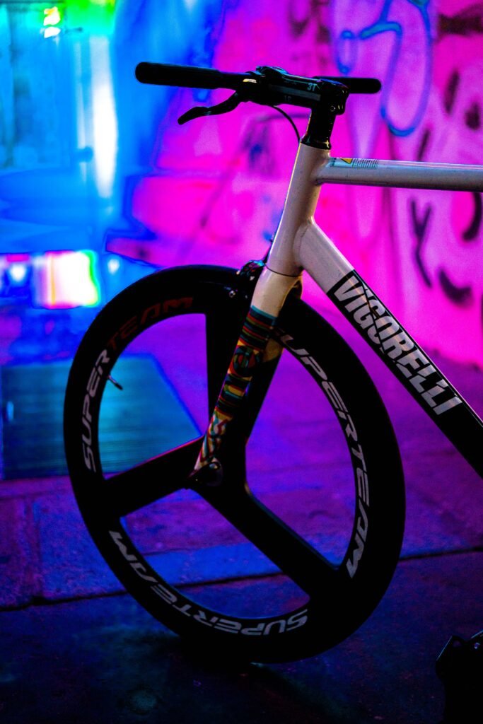 Roue avant trois bâtons et fourche Cinelli sous des lumières roses et bleues.