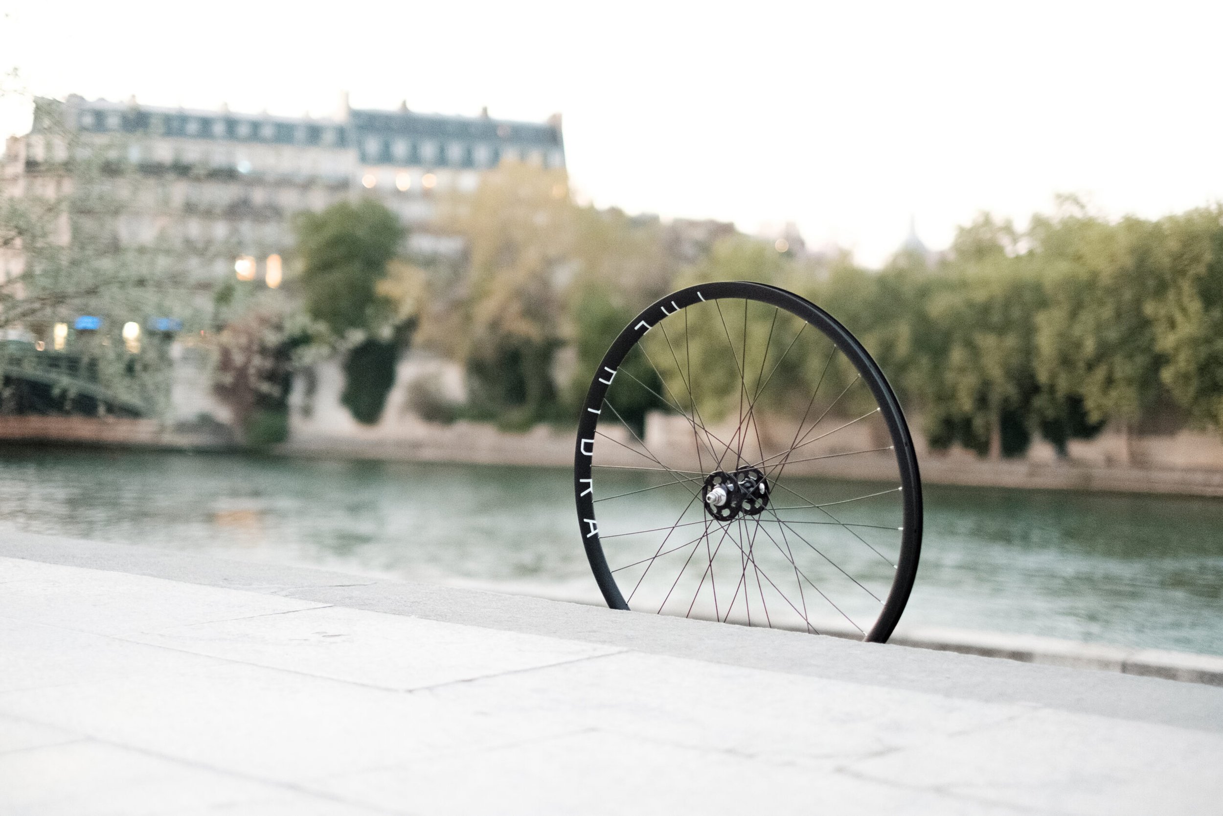 Roue noire fraîchement rayonnée, posée au bord de la Seine.