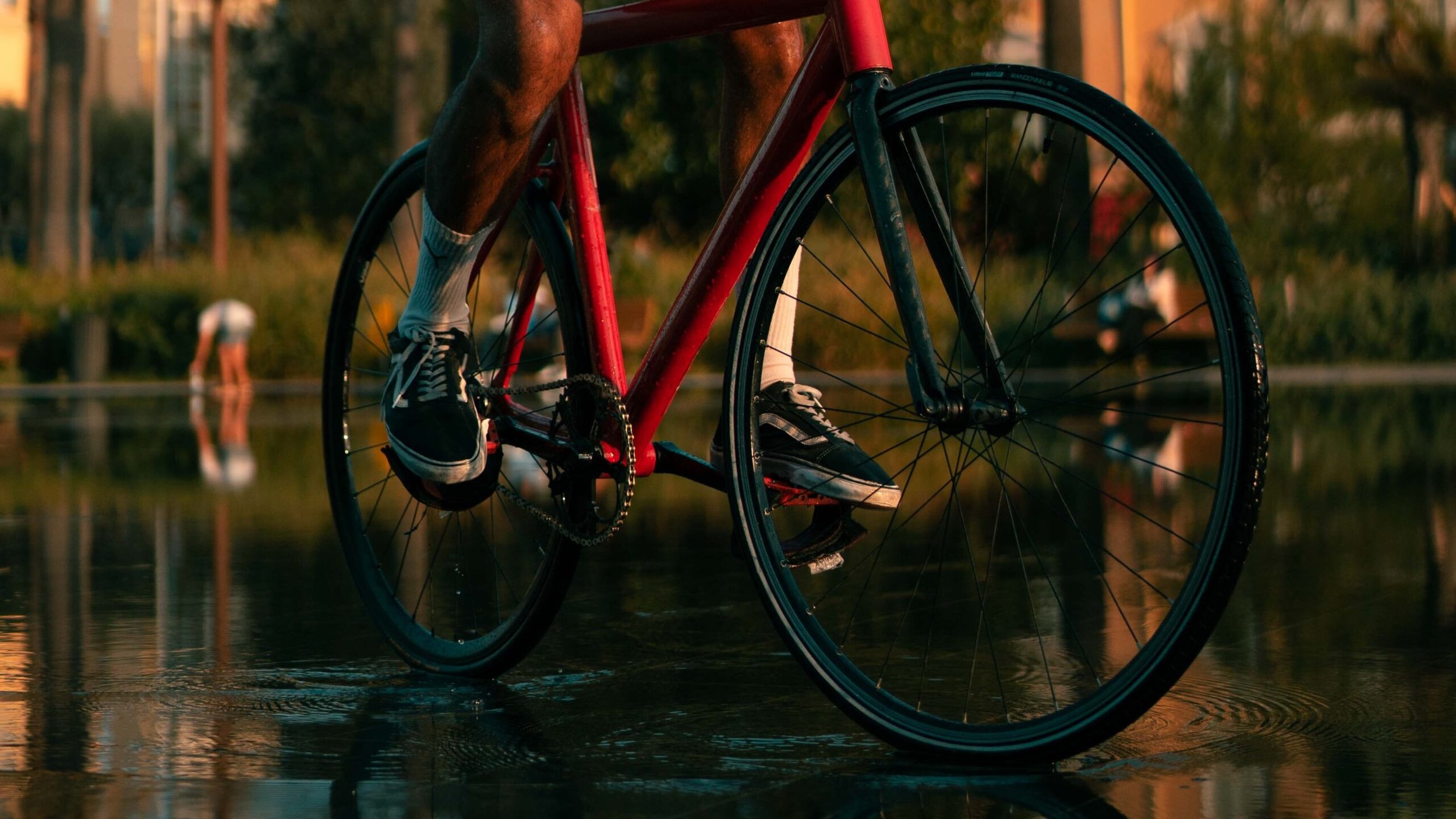 Gros plan sur les roues et les pédales d’un vélo rouge et leur reflet dans l’eau.