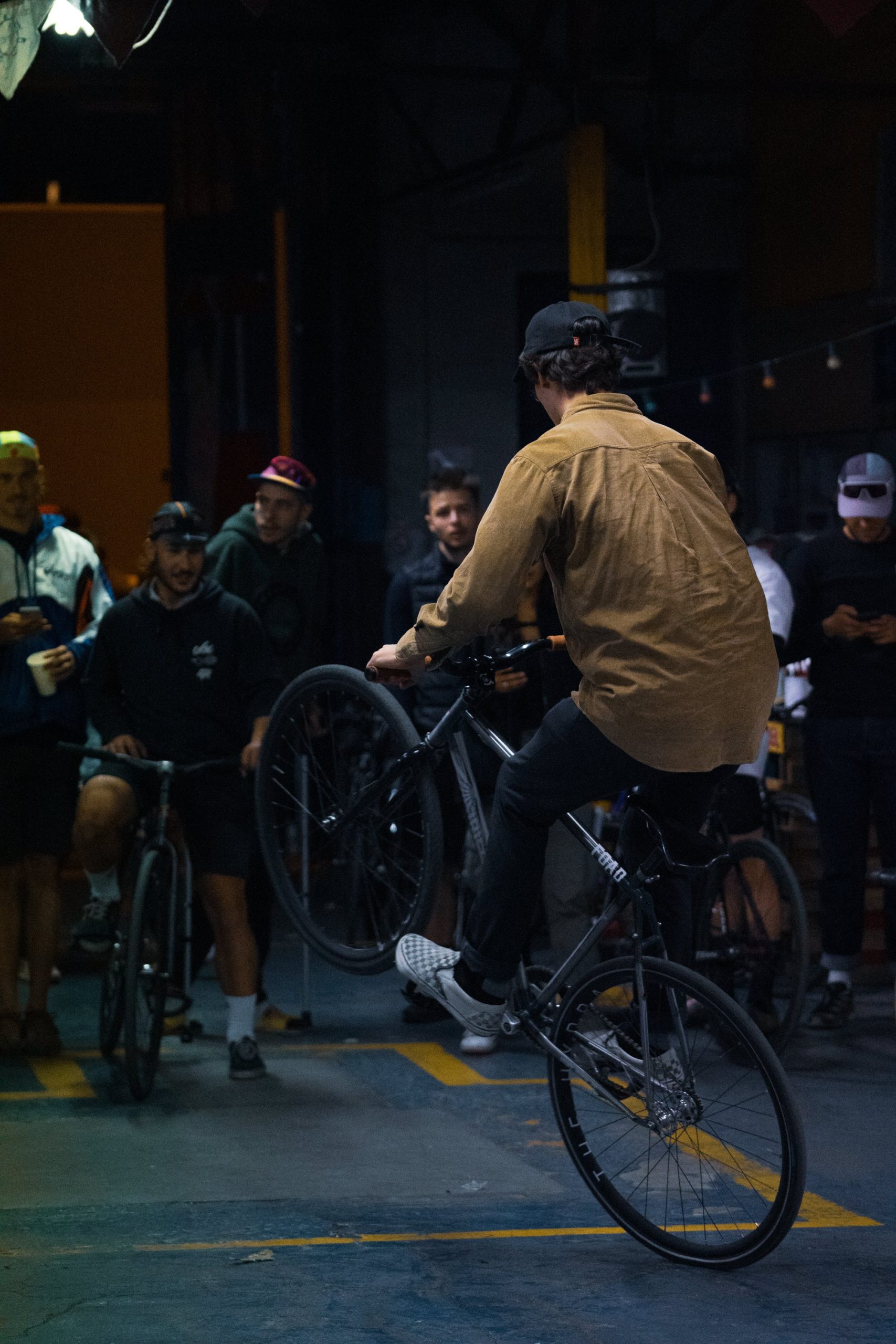 Rider levant la roue avant lors d’une session de nuit, entouré d’autres riders.
