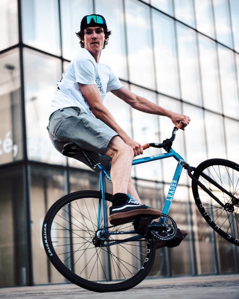 Rider en T-shirt blanc en équilibre sur un fixie bleu.