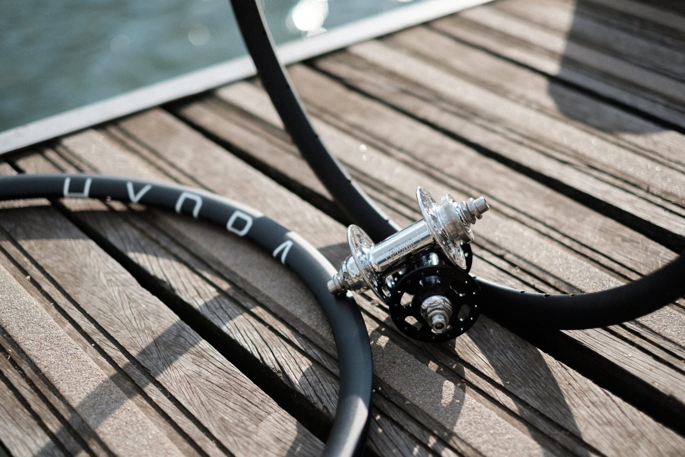 Paire de roues de fixie noires avec moyeu arrière argenté, sur une terrasse en bois.