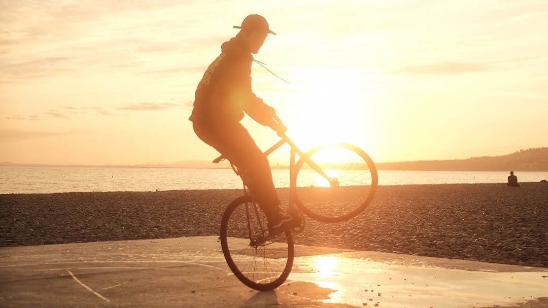 Rider en équilibre sur la roue arrière au bord de l’eau, au coucher du soleil.