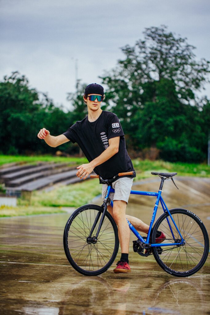 Rider en équilibre sur un vélo bleu, une main levée, près d’une fontaine.